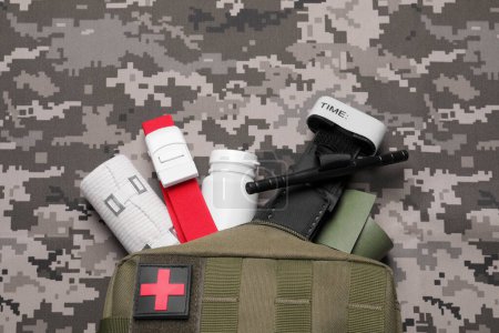 Photo for First aid kit with medical tourniquet, pills and bands on military fabric, flat lay - Royalty Free Image