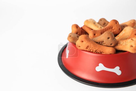 Téléchargez les photos : Biscuits pour chiens en forme d'os dans un bol d'alimentation sur fond blanc, gros plan. Espace pour le texte - en image libre de droit