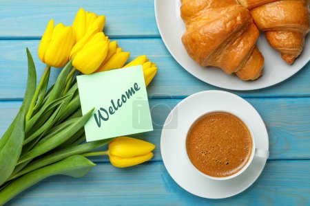 Téléchargez les photos : Welcome card, beautiful yellow tulips, croissants and cup of aromatic coffee on light blue wooden table, flat lay - en image libre de droit
