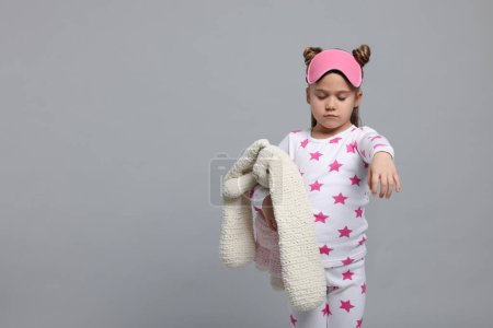 Téléchargez les photos : Girl in pajamas and sleep mask with toy bunny sleepwalking on gray background, space for text - en image libre de droit