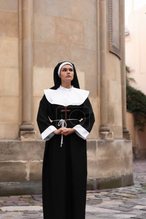 Téléchargez les photos : Jeune religieuse avec croix chrétienne près du bâtiment à l'extérieur - en image libre de droit