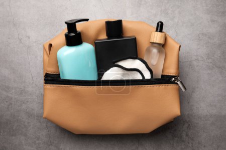 Photo for Preparation for spa. Compact toiletry bag with different cosmetic products on grey textured background, top view - Royalty Free Image