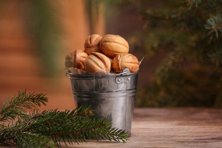 Téléchargez les photos : Metal bucket of delicious nut shaped cookies and fir branches on wooden table, space for text - en image libre de droit
