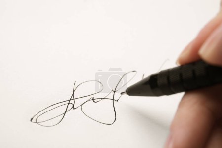 Woman writing her signature with pen on sheet of white paper, closeup