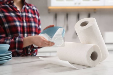 Woman wiping bowl with paper towel at white marble table in kitchen, selective focus. Space for text