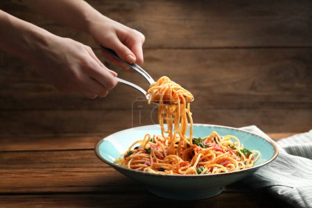 Woman eating delicious pasta at wooden table, closeup