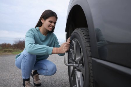 Young woman changing tire of car outdoors