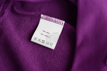 White clothing label with care information on purple garment, top view