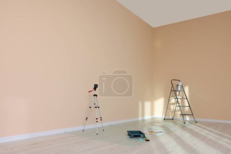 Téléchargez les photos : Escalier, niveau laser et outils de peinture près du mur dans une pièce vide, espace pour le texte - en image libre de droit