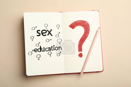 Notizbuch mit Text Sexualerziehung, Fragezeichen, weibliche und männliche Geschlechtszeichen auf beigem Hintergrund, Draufsicht