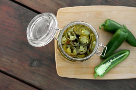 Fresh and pickled green jalapeno peppers on wooden table, top view