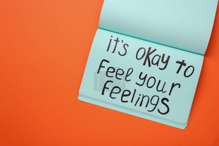 Téléchargez les photos : Notebook avec phrase It's Okay To Feel Your Feelings sur fond orange, vue du dessus. Espace pour le texte - en image libre de droit