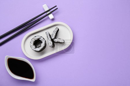 Foto de Palabra Ok hecha de rollos de sushi, palillos y salsa de soja sobre fondo violeta, puesta plana. Espacio para texto - Imagen libre de derechos