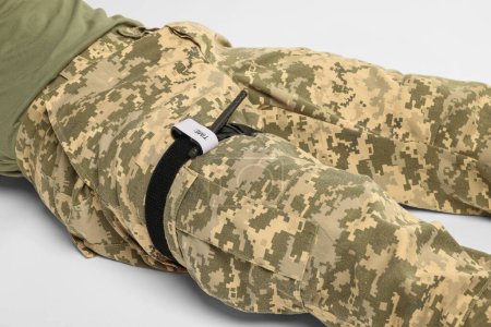 Soldat en uniforme militaire avec garrot médical sur la jambe sur fond blanc, gros plan