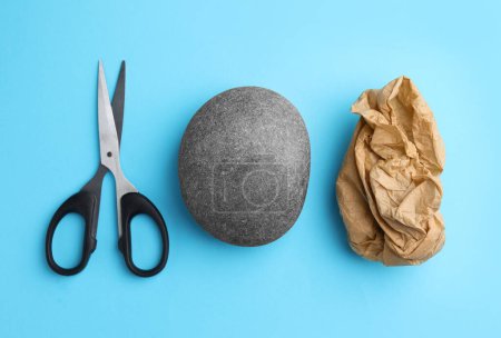 Rock, crumpled paper and scissors on light blue background, flat lay