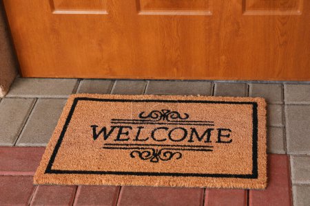 Foto de Door mat with word Welcome on street tiles near entrance - Imagen libre de derechos