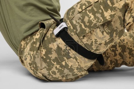 Soldat in Militäruniform mit medizinischem Tourniquet am Bein vor weißem Hintergrund, Nahaufnahme