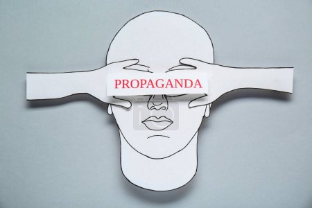 Information warfare. Human closing eyes with hands and card with word Propaganda. Paper cutouts on light grey background, top view
