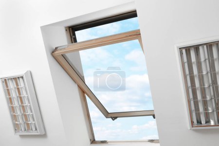Ventana abierta del techo del tragaluz en el techo inclinado en la habitación del ático, vista inferior