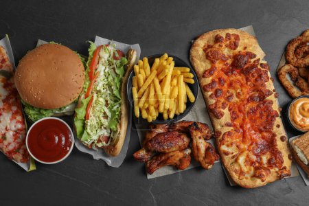 Foto de Hamburguesa, pizza y otra comida rápida en la mesa negra, puesta plana - Imagen libre de derechos
