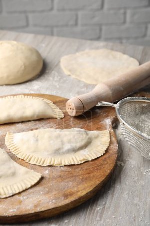 Raw chebureki with tasty filling and rolling pin on wooden table