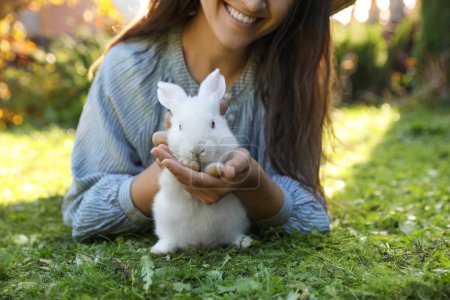 Foto de Mujer feliz con lindo conejo en la hierba verde al aire libre, primer plano - Imagen libre de derechos