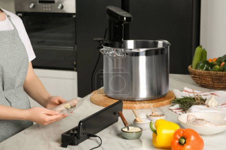 Woman using sealer for vacuum packing in kitchen, closeup. Sous vide cooking