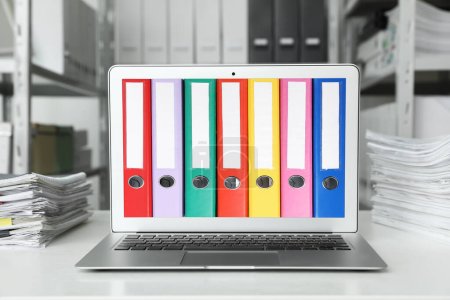 Informationen speichern und organisieren. Moderner Laptop mit gebundenen Büromappen auf dem Bildschirm im Archivraum