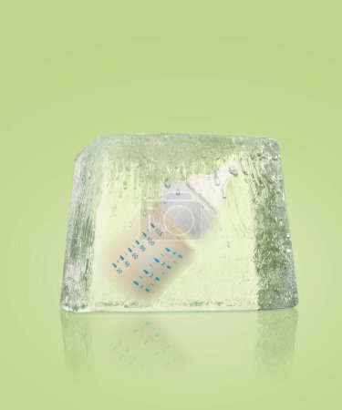 Foto de Conservación del material genético. Bebé biberón en cubo de hielo como criopreservación sobre fondo verde claro - Imagen libre de derechos