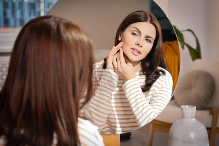 Photo for Young woman looking in mirror and squeezing pimple indoors. Hormonal disorders - Royalty Free Image
