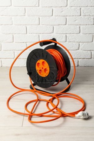 Photo for Extension cord reel on floor near white brick wall. Electrician's equipment - Royalty Free Image