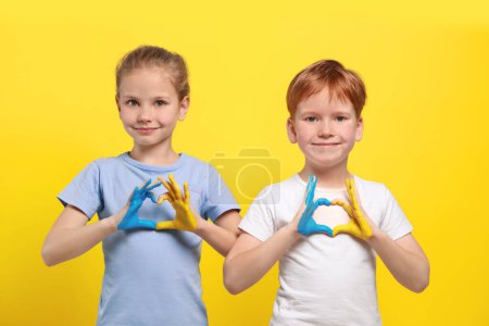 Photo for Little girl and boy making heart with their hands painted in Ukrainian flag colors on yellow background. Love Ukraine concept - Royalty Free Image