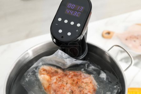 Sous vide cooker and vacuum packed meat in pot on white table, closeup. Thermal immersion circulator