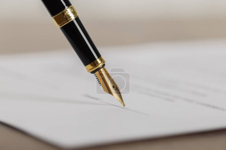 Writing on document with fountain pen at wooden table, closeup. Notary contract