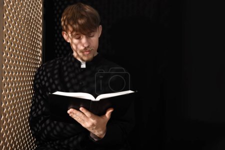 Téléchargez les photos : Prêtre catholique avec Bible près de la fenêtre en bois dans le confessionnal. Espace pour le texte - en image libre de droit