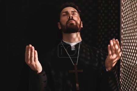 Foto de Sacerdote católico en sotana orando a Dios en cabina confesional - Imagen libre de derechos