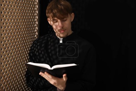 Foto de Sacerdote católico con Biblia cerca de ventana de madera en confesionario. Espacio para texto - Imagen libre de derechos