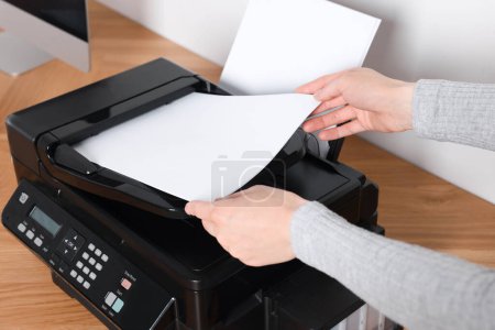 Téléchargez les photos : Woman loading paper into printer at wooden table indoors, closeup - en image libre de droit