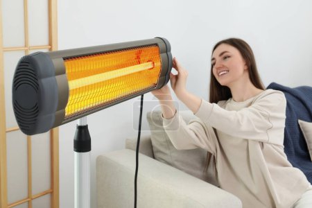 Woman adjusting temperature on electric infrared heater indoors