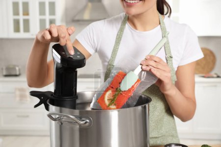 Mujer poniendo salmón envasado al vacío en olla y el uso de circulador de inmersión térmica en la cocina, primer plano. Sous vide cocinar