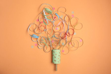 Photo for Beautiful serpentine and confetti bursting out of party popper on coral background, flat lay - Royalty Free Image