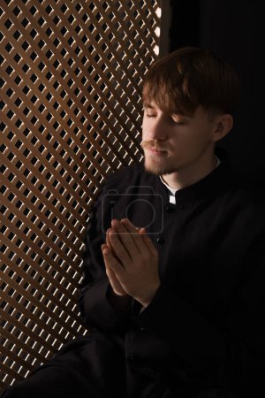 Téléchargez les photos : Prêtre catholique priant près d'une cloison en bois au confessionnal - en image libre de droit