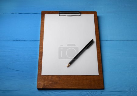 Téléchargez les photos : Presse-papiers avec feuille de papier et stylo sur table en bois bleu clair. Espace pour le texte - en image libre de droit