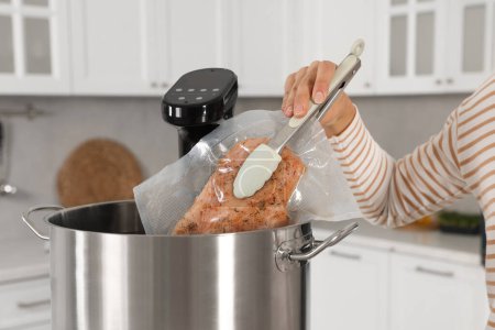Foto de Mujer poniendo carne envasada al vacío en la olla con sous cocina vide en la cocina, primer plano. Circulador de inmersión térmica - Imagen libre de derechos