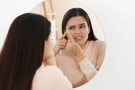 Téléchargez les photos : Jeune femme serrant bouton près du miroir à l'intérieur. Affections hormonales - en image libre de droit