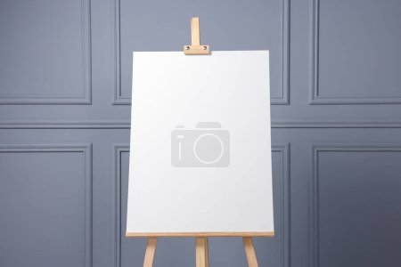 Photo for Wooden easel with blank canvas near grey wall indoors, closeup. Space for text - Royalty Free Image