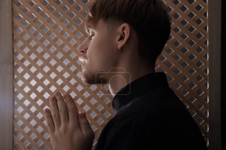 Téléchargez les photos : Prêtre catholique priant près d'une fenêtre en bois dans une cabine confessionnelle - en image libre de droit