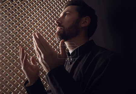 Téléchargez les photos : Prêtre catholique en soutane priant Dieu en cabine confessionnelle - en image libre de droit