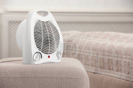 Modern electric fan heater on pouf in cozy room. Space for text