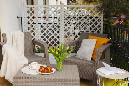 Téléchargez les photos : Différents oreillers, couverture, petit déjeuner et belles tulipes sur rotin meubles de jardin en plein air - en image libre de droit